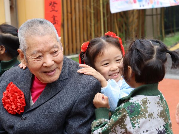 兩位孩子正在為爺爺捶背。新絲路幼兒園供圖